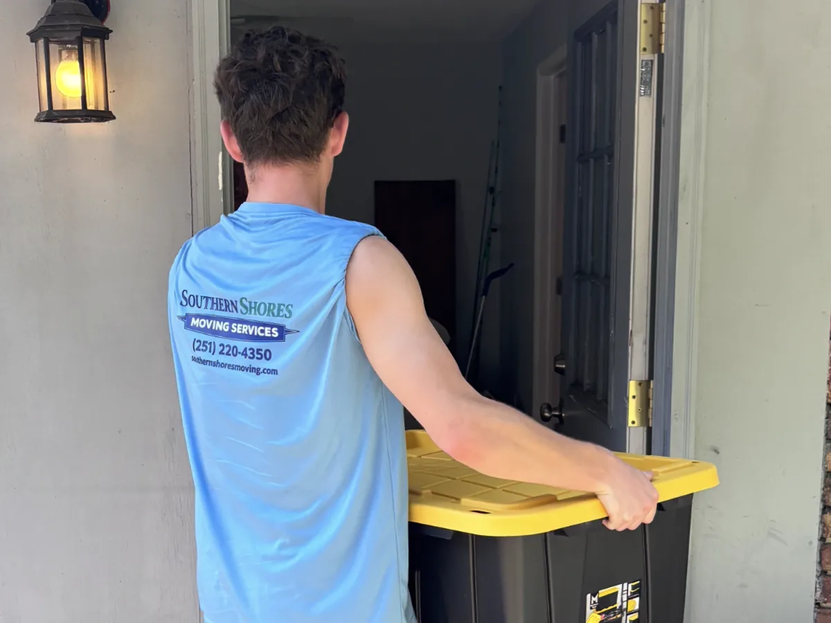Southern Shores Moving mover carrying a packed storage tote through a front doorway during a move in Milton, Florida