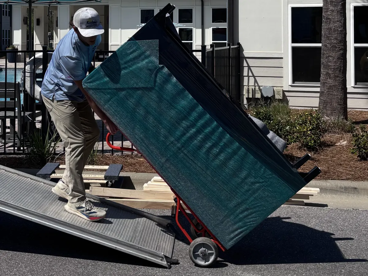 Southern Shores Moving mover wheeling a shrink-wrapped dresser up a truck ramp on a hand truck during a move in Pensacola, Florida