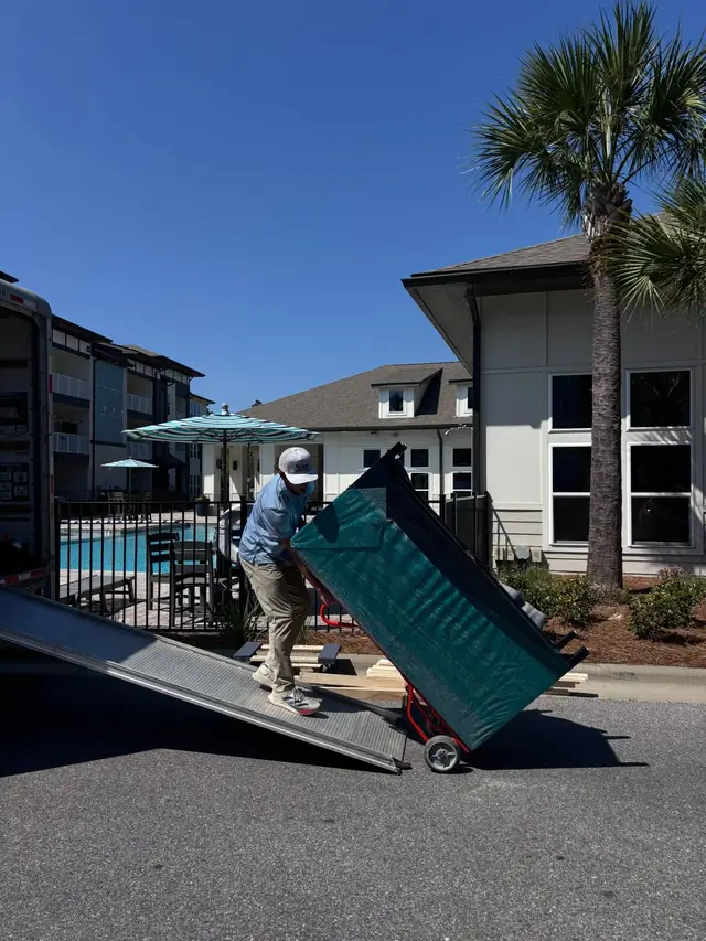 Mover rolling furniture on a dolly down a truck ramp at an apartment complex
