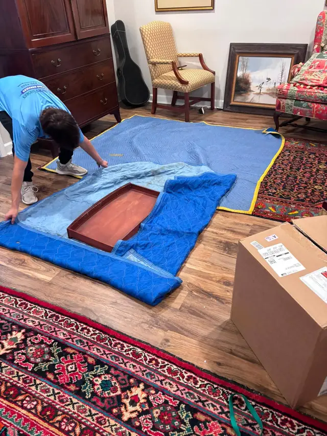 Mover spreading out blue moving blankets on a rug