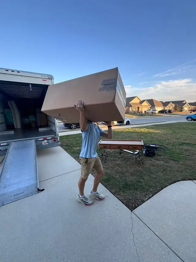 Mover carrying a large box down a truck ramp at sunset