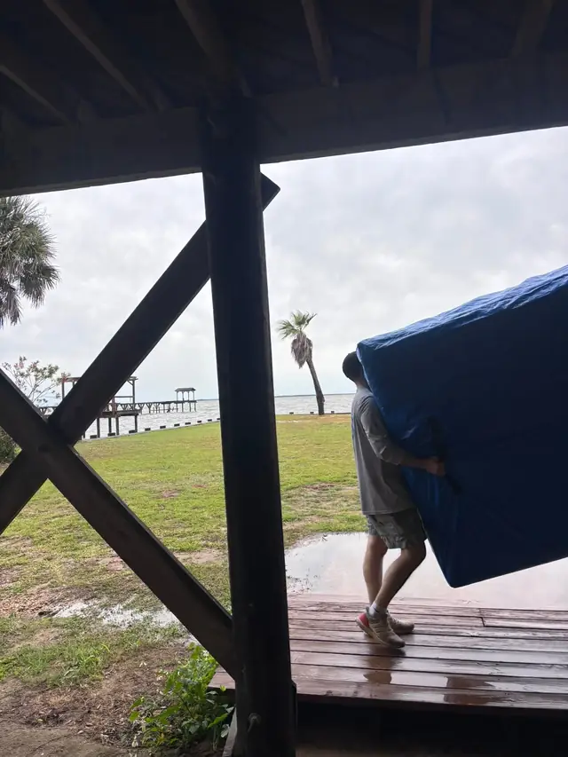 Mover carrying padded furniture across a deck by the water