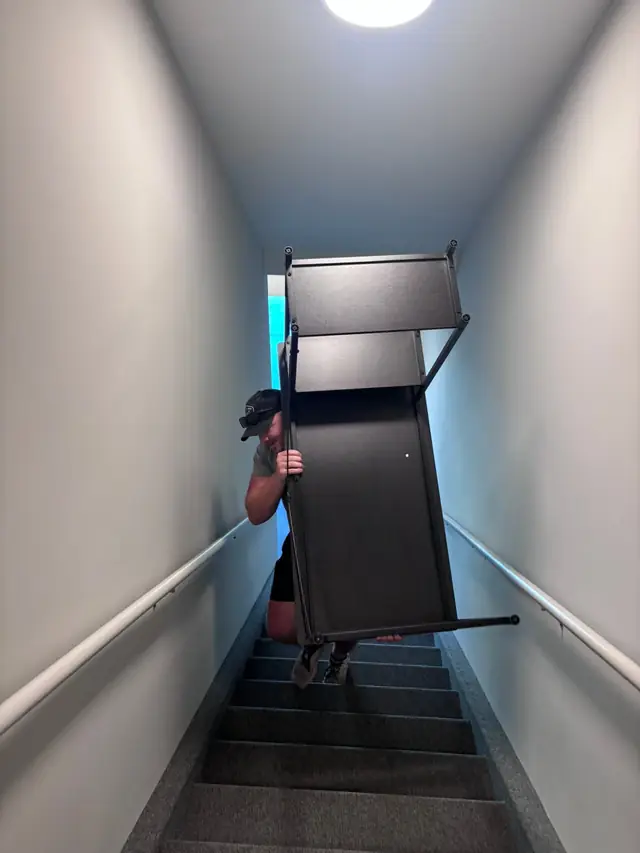 Mover carrying furniture down a narrow stairwell