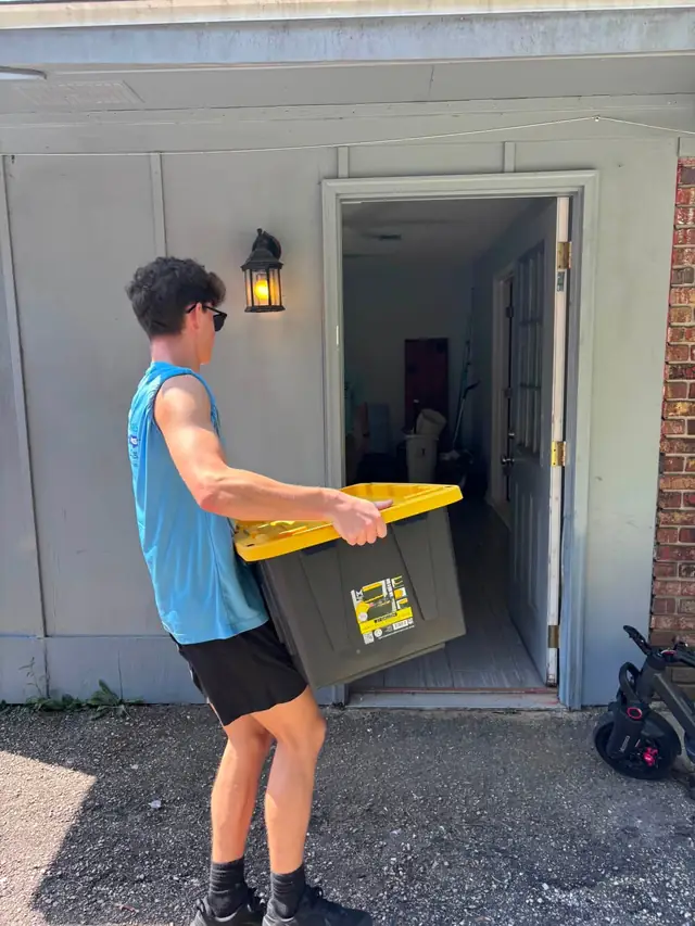 Mover carrying a storage tote out of a house