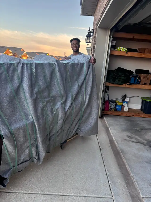 Mover holding padded furniture upright in a garage