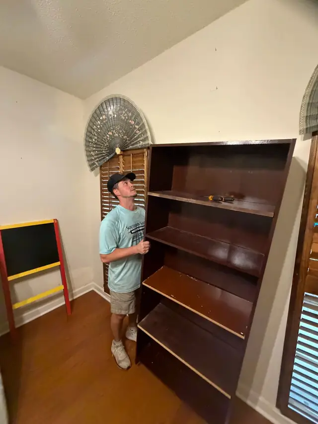 Mover positioning a wooden bookshelf in a bedroom