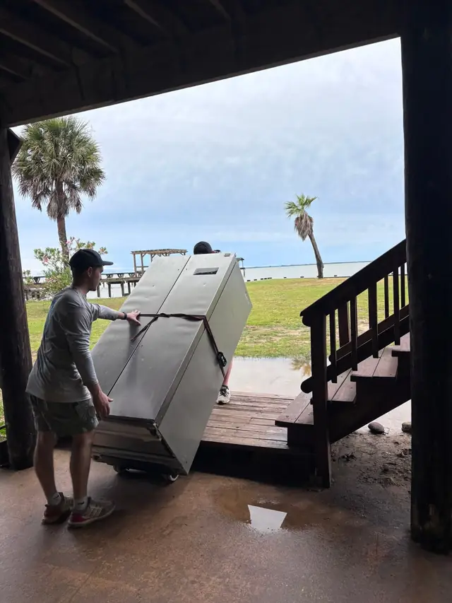 Movers carrying a padded appliance down the steps of a waterfront home