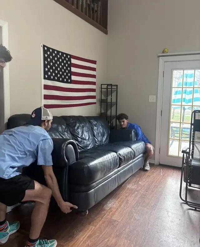 Movers carrying a leather sofa through a living room