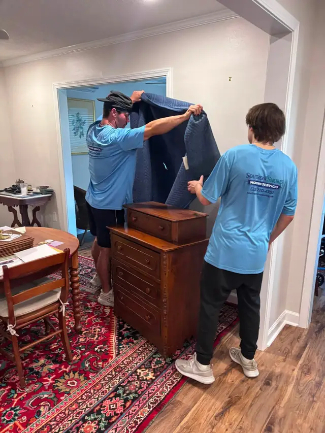 Two movers wrapping a wooden chest in moving blankets