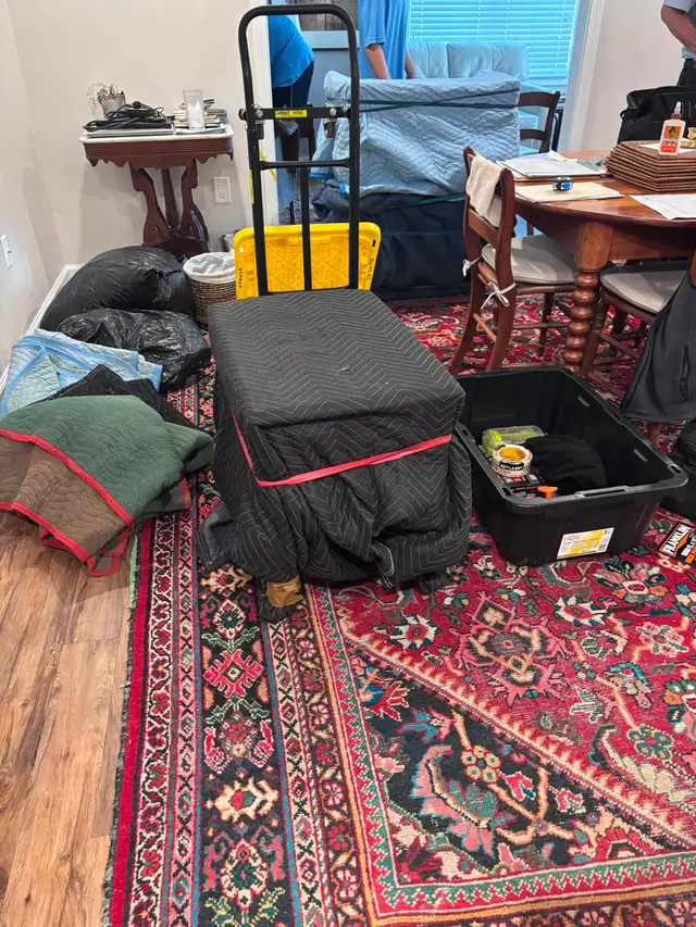 Room staged with wrapped furniture, totes and a dolly ready to load